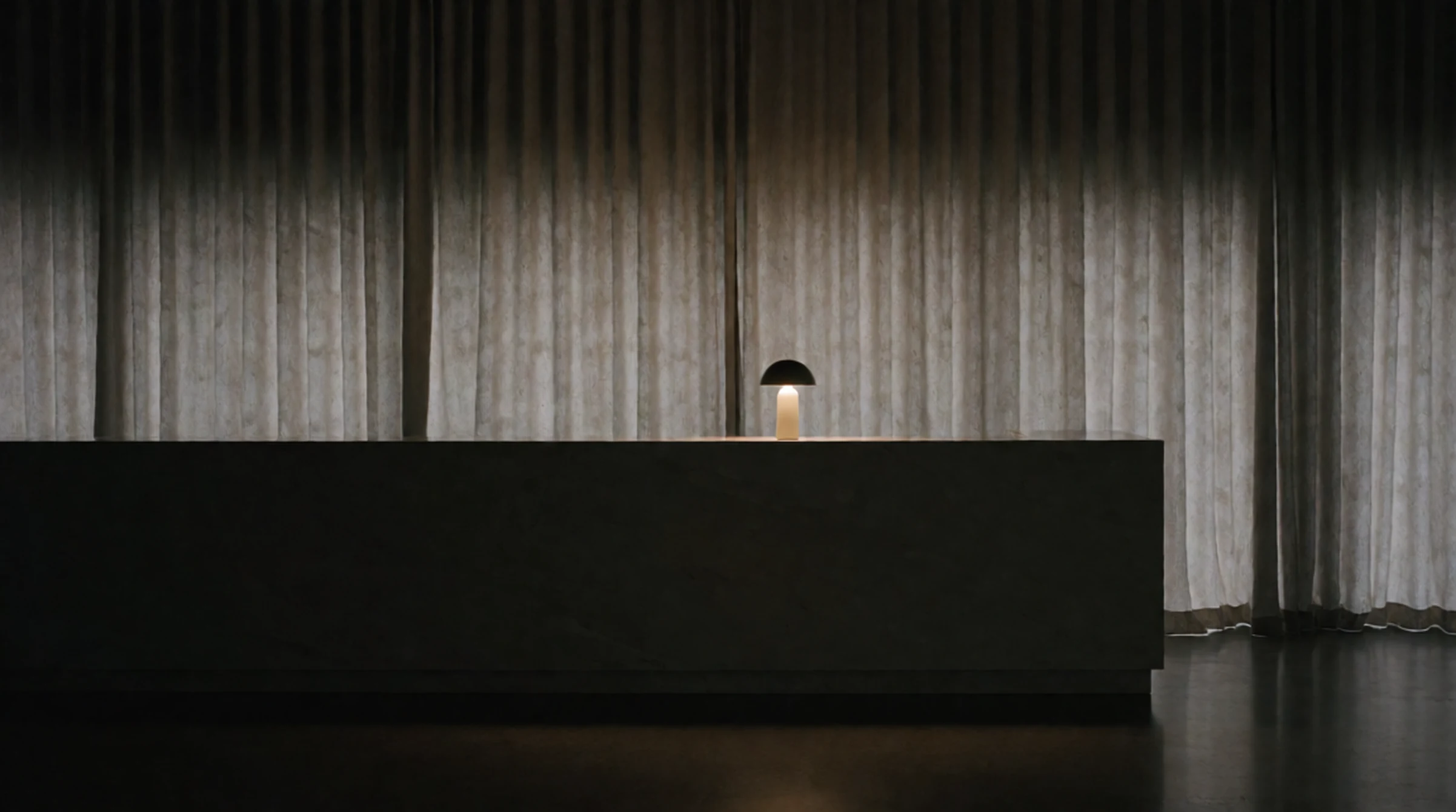Modern desk with a glowing mushroom-shaped lamp in a dim room with sheer curtains.